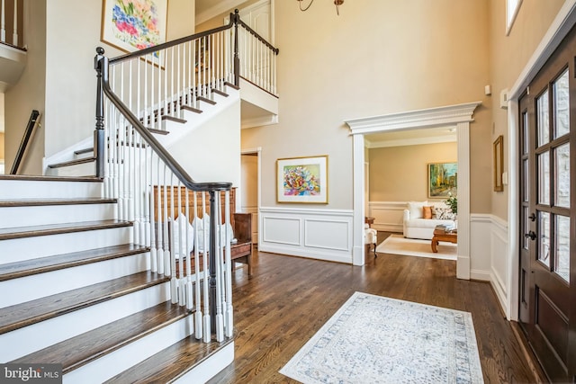 entrance foyer with a high ceiling, dark wood-style flooring, and wainscoting