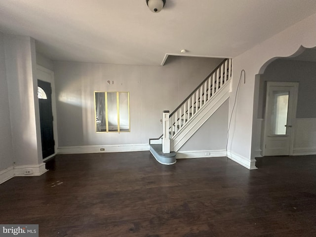 unfurnished living room with dark wood-type flooring, arched walkways, stairway, and baseboards