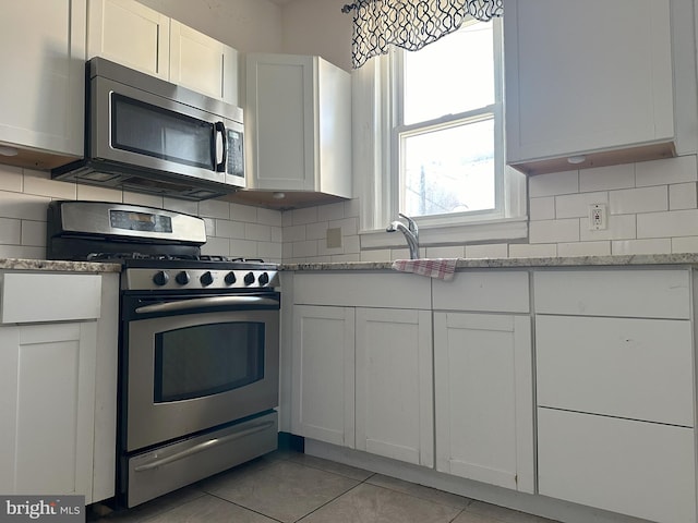 kitchen with appliances with stainless steel finishes, light stone countertops, white cabinetry, and tasteful backsplash