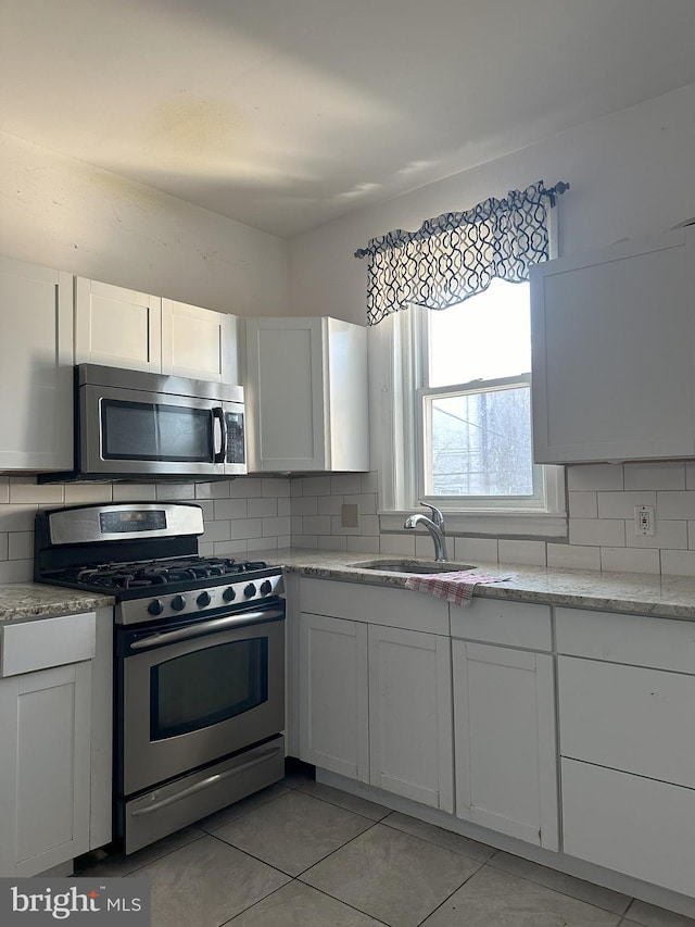 kitchen featuring stainless steel appliances, white cabinets, a sink, and decorative backsplash