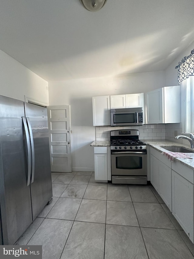 kitchen featuring appliances with stainless steel finishes, a sink, light stone countertops, and white cabinets