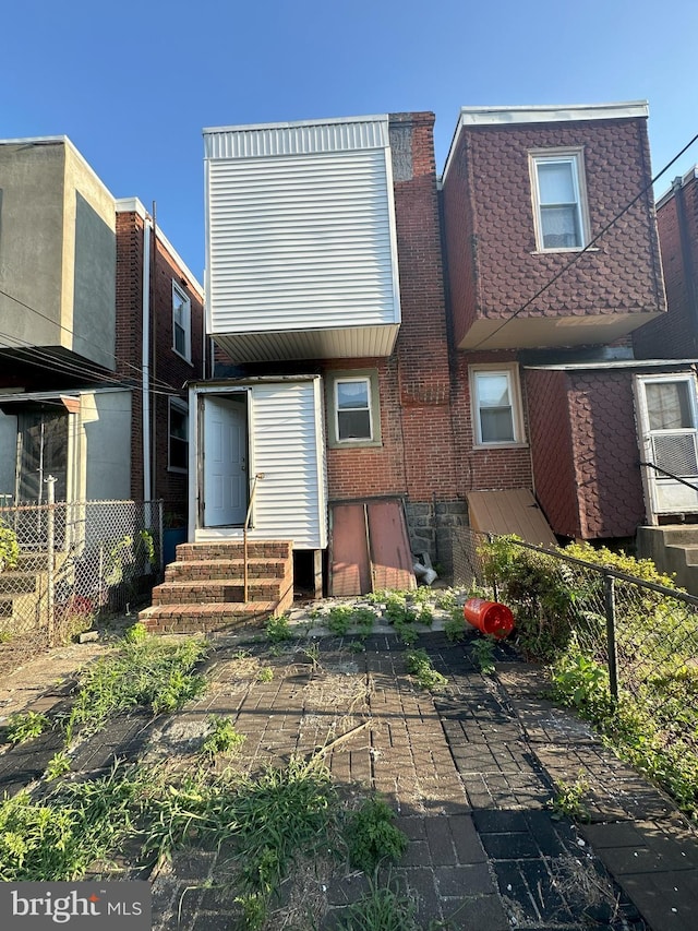 back of property featuring entry steps, brick siding, and fence