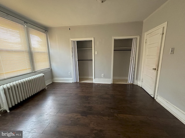 unfurnished bedroom with dark wood-style floors, baseboards, radiator heating unit, and two closets