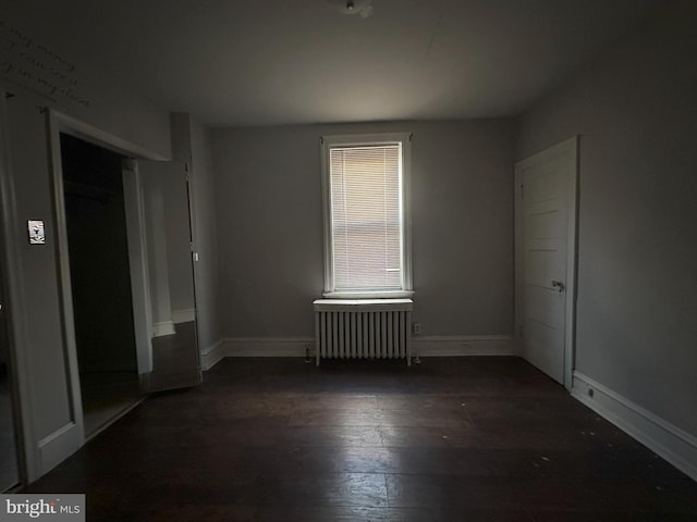 unfurnished bedroom featuring dark wood-type flooring, a closet, baseboards, and radiator heating unit