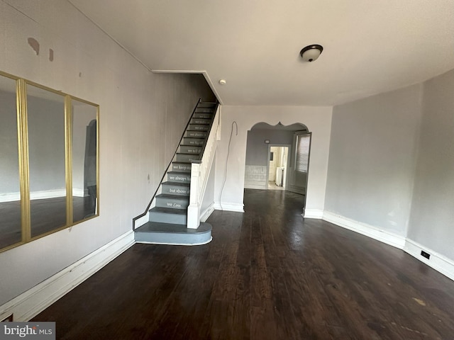 interior space featuring arched walkways, dark wood finished floors, baseboards, and stairs