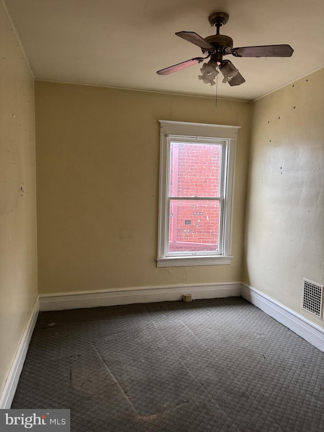 empty room with dark colored carpet, a ceiling fan, visible vents, and baseboards