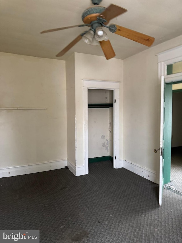 unfurnished bedroom with baseboards, dark colored carpet, and a ceiling fan