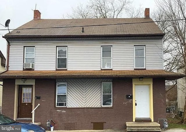 view of front facade with entry steps, brick siding, and a chimney