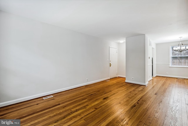 unfurnished room featuring baseboards, wood finished floors, visible vents, and a notable chandelier