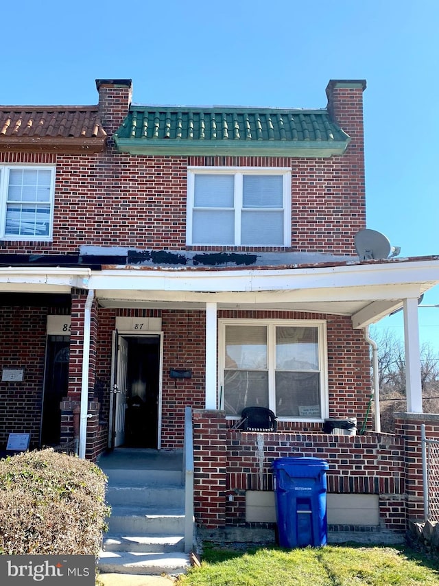 view of property with covered porch, brick siding, and a chimney