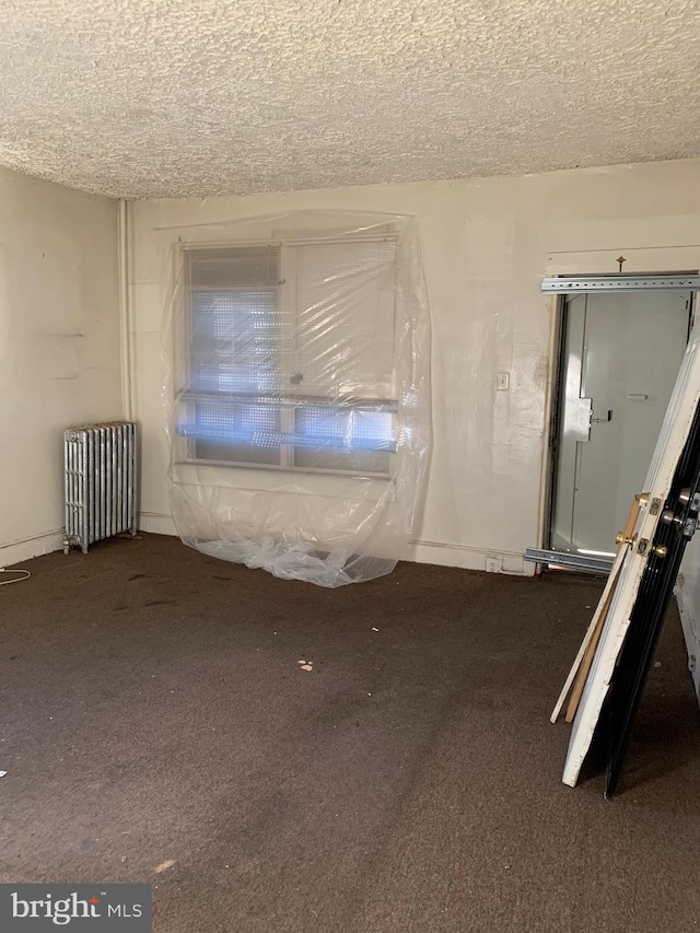 carpeted spare room featuring a textured ceiling and radiator heating unit