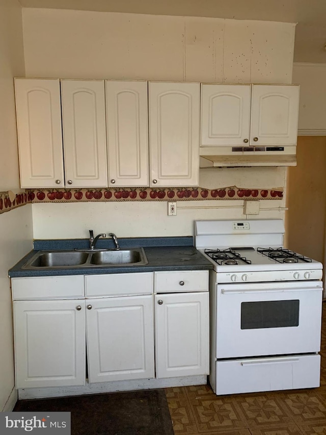 kitchen with under cabinet range hood, a sink, gas range gas stove, dark countertops, and white cabinetry