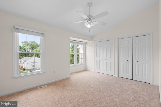 unfurnished bedroom featuring carpet floors, two closets, lofted ceiling, visible vents, and baseboards