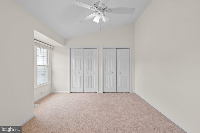 unfurnished bedroom featuring ceiling fan, baseboards, vaulted ceiling, multiple closets, and carpet