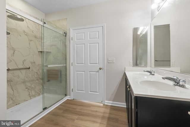 full bathroom featuring double vanity, a marble finish shower, a sink, and wood finished floors