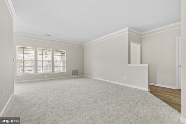 carpeted spare room featuring visible vents, crown molding, and baseboards