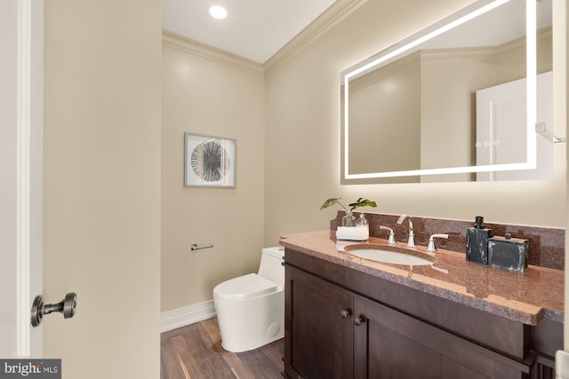 half bathroom featuring toilet, wood finished floors, vanity, baseboards, and crown molding