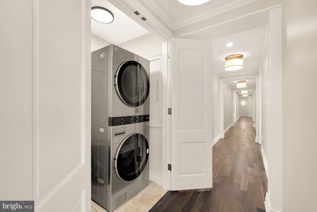 laundry room featuring laundry area, baseboards, stacked washer and clothes dryer, wood finished floors, and crown molding