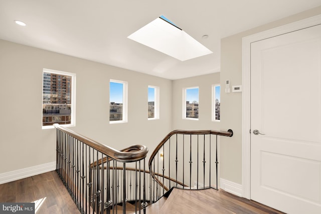 hallway featuring a skylight, baseboards, wood finished floors, an upstairs landing, and recessed lighting