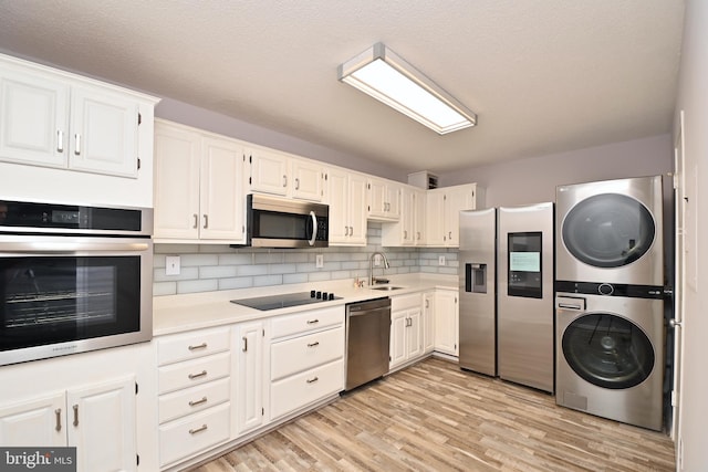 kitchen with white cabinets, appliances with stainless steel finishes, stacked washer / drying machine, light countertops, and a sink