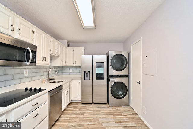 kitchen with stacked washer and dryer, a sink, white cabinets, light countertops, and appliances with stainless steel finishes