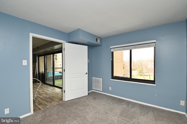 unfurnished room featuring a textured ceiling, carpet floors, visible vents, and baseboards