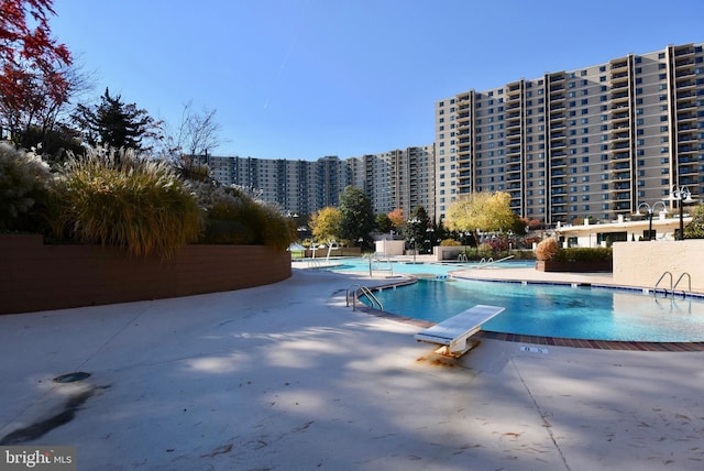 community pool featuring a patio area, a view of city, fence, and a diving board