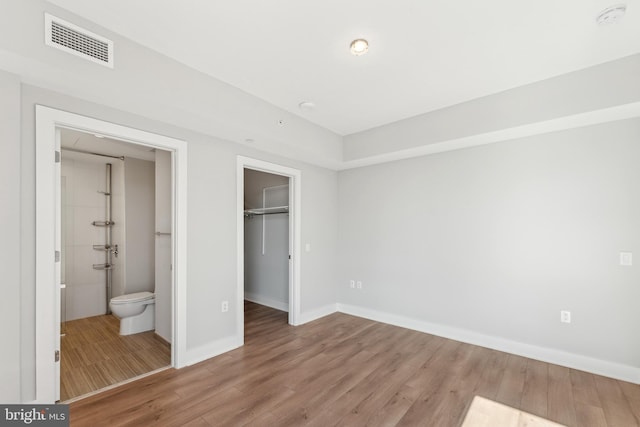 unfurnished bedroom featuring a closet, visible vents, a spacious closet, light wood-style floors, and baseboards