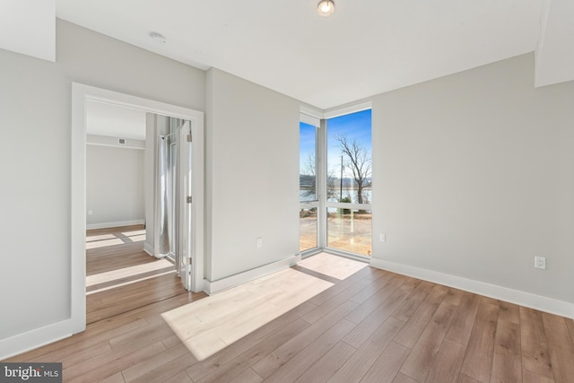 spare room featuring light wood-type flooring, baseboards, and a wall of windows