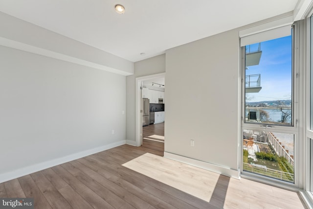 unfurnished room featuring light wood-type flooring, expansive windows, and baseboards