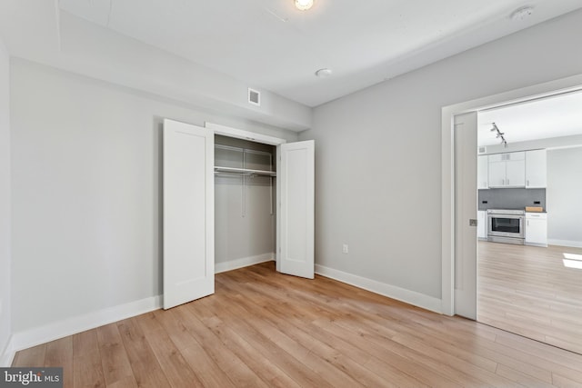 unfurnished bedroom featuring light wood-style floors, baseboards, visible vents, and a closet