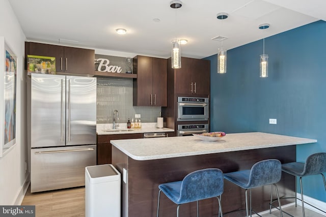 kitchen with stainless steel appliances, a sink, light wood-style floors, hanging light fixtures, and light countertops