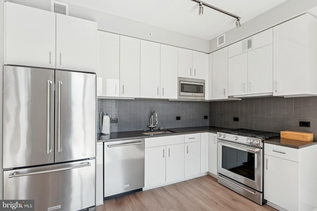 kitchen featuring appliances with stainless steel finishes, dark countertops, a sink, and white cabinetry