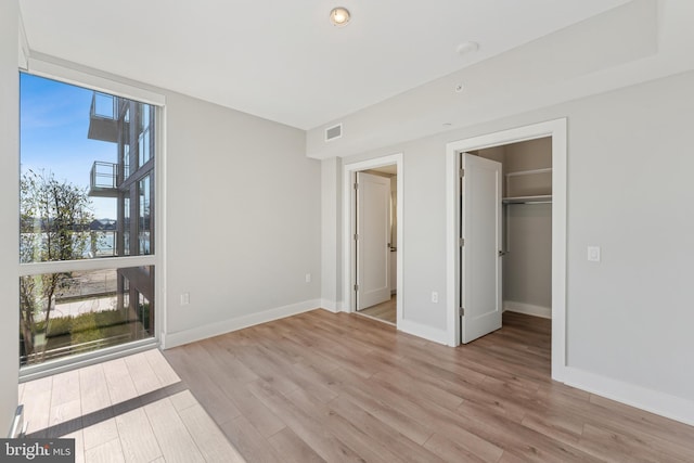 unfurnished bedroom featuring visible vents, baseboards, light wood-style floors, a spacious closet, and a wall of windows