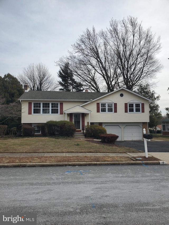 raised ranch with a garage, a chimney, a front lawn, and aphalt driveway