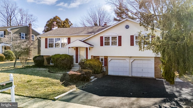 split foyer home featuring driveway, a garage, a front lawn, and brick siding