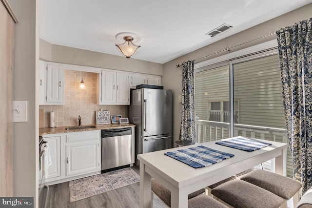 kitchen with a sink, visible vents, white cabinets, appliances with stainless steel finishes, and light stone countertops