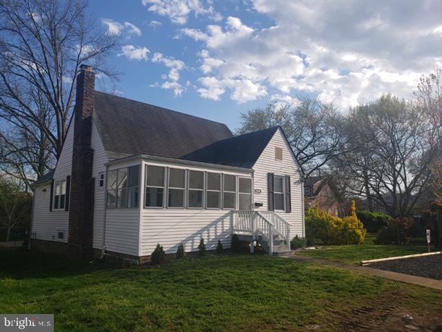 view of front facade with a front yard, a sunroom, and a chimney