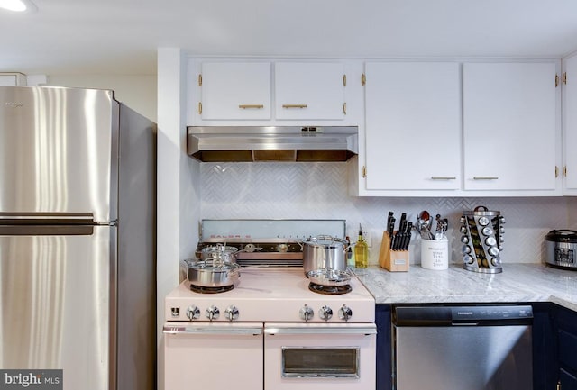 kitchen with tasteful backsplash, white cabinets, appliances with stainless steel finishes, light stone countertops, and extractor fan