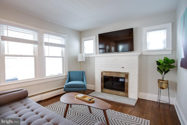 living room featuring baseboard heating, a brick fireplace, wood finished floors, and baseboards