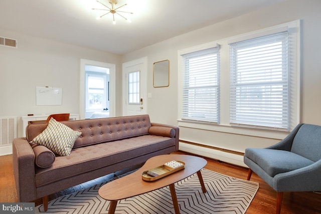 living room featuring a baseboard heating unit, wood finished floors, and visible vents