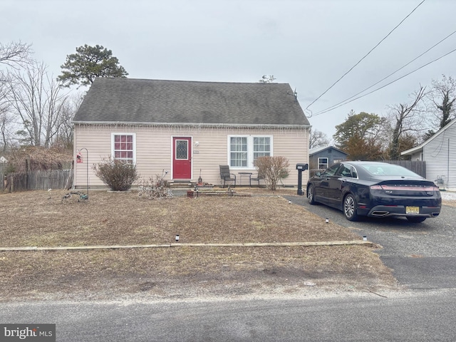 view of front facade featuring entry steps, roof with shingles, driveway, and fence