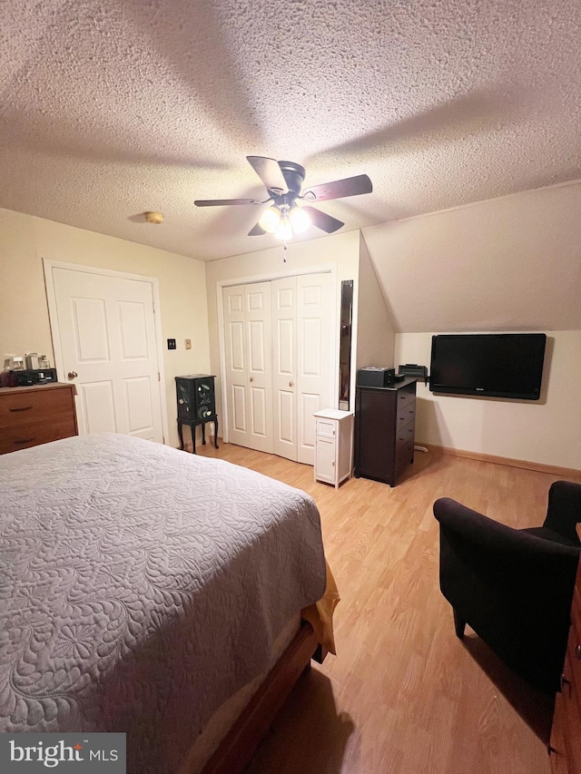 bedroom featuring a textured ceiling, lofted ceiling, a ceiling fan, a closet, and light wood finished floors