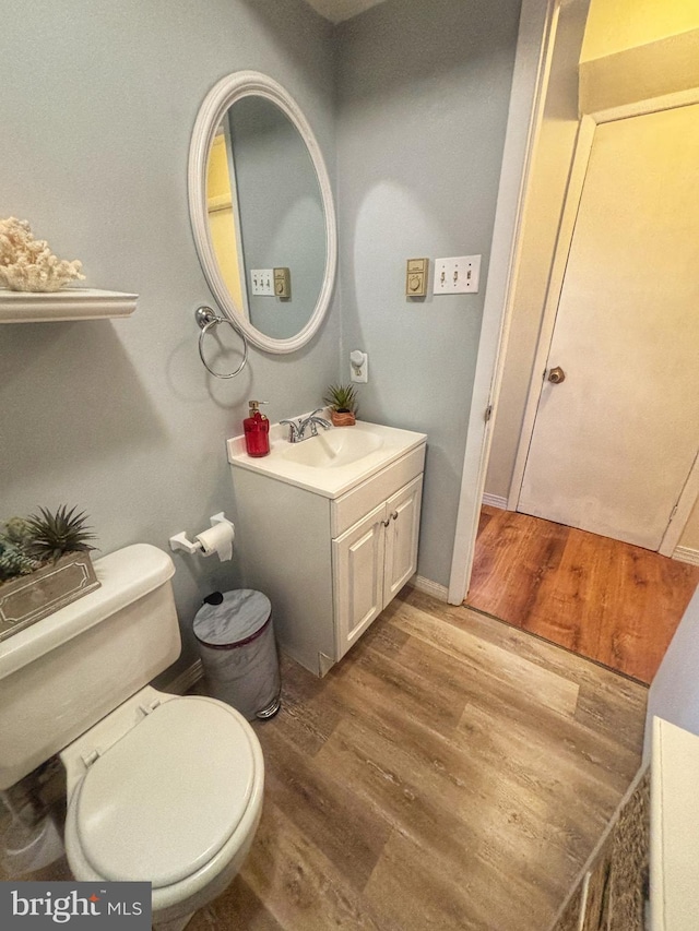 half bathroom with toilet, wood finished floors, and vanity