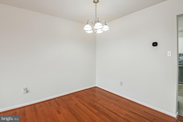 spare room with a notable chandelier, baseboards, and wood finished floors