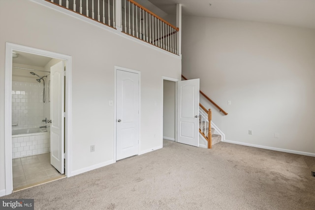 unfurnished living room with light colored carpet, a towering ceiling, baseboards, and stairs