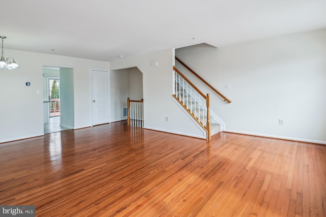 unfurnished living room featuring baseboards, stairway, hardwood / wood-style flooring, and an inviting chandelier