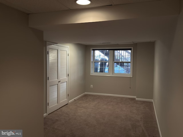 unfurnished bedroom featuring carpet floors, baseboards, a drop ceiling, and a closet