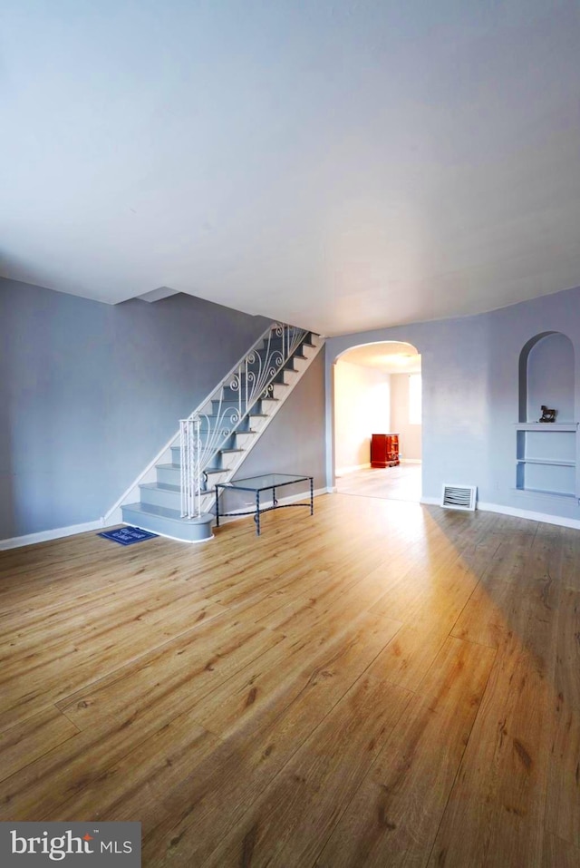 living room featuring arched walkways, visible vents, wood finished floors, baseboards, and stairs