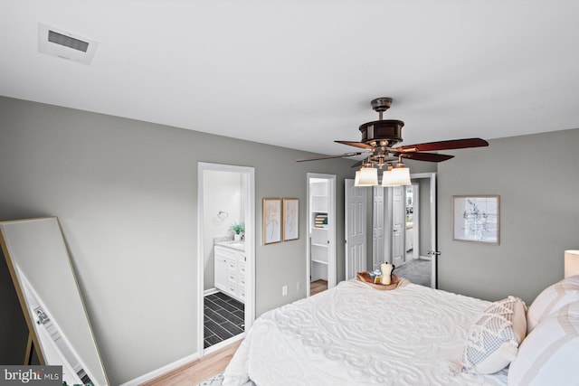 bedroom with light wood-type flooring, visible vents, baseboards, and ensuite bath